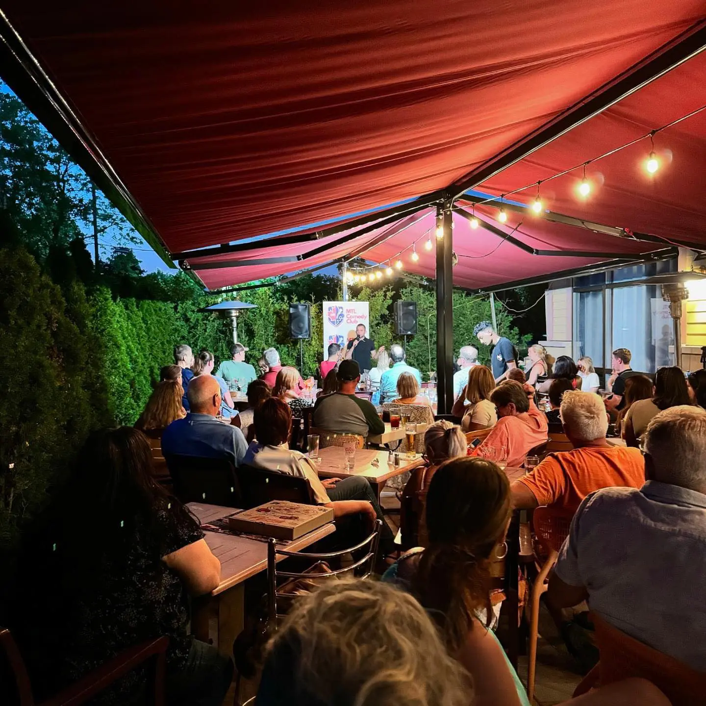 Image20250424143052 A group of people sitting at tables under an awning.
